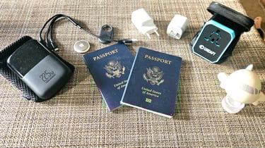 Portable charger, charging cables, luggage tracker, universal adapter and USB wall chargers on table