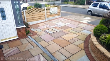 Colourful sandstone paving driveway and curved raised planter with colourful plants and flowers