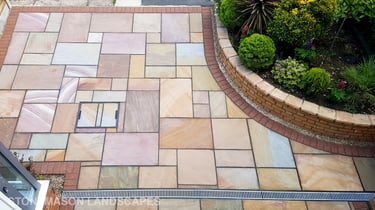 Colourful sandstone paving driveway and curved raised planter with colourful plants and flowers
