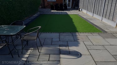 Fully paved grey sandstone patio with charcoal edging bocks and artificial grass lawn
