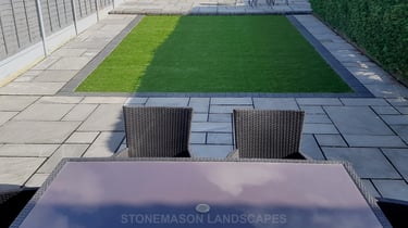 Fully paved grey sandstone patio with charcoal edging bocks and artificial grass lawn