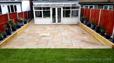Large sandstone patio and raised wooden sleeper planters