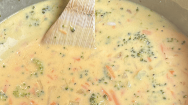 Broccoli Cheddar Soup in a pot with a wooden spoon sitting there.