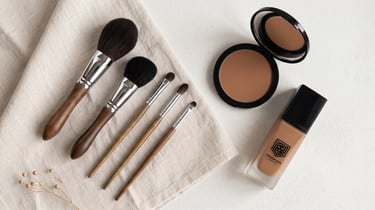 Yeshua Skin liquid foundation, bronzer, and wood-handled makeup brushes on a neutral linen cloth.