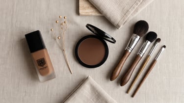 Yeshua Skin liquid foundation and bronzer compact with professional wooden makeup brushes on linen fabric.