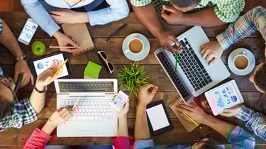 a group of people sitting around a table with laptops