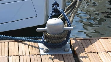 Cime di ormeggio nautiche blu fissate a un bitta di metallo accanto a una barca di lusso.