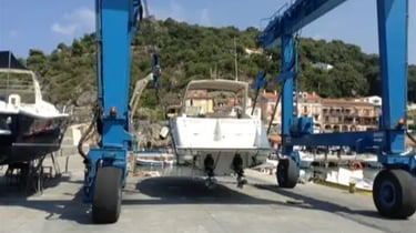 Un travel lift marino blu solleva dall'acqua un motoscafo per portarlo in servizio in cantiere