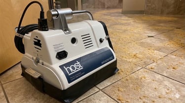 A professional-grade white Host ExtractorVAC machine cleaning loose, dirt-lifting compound from a tiled floor