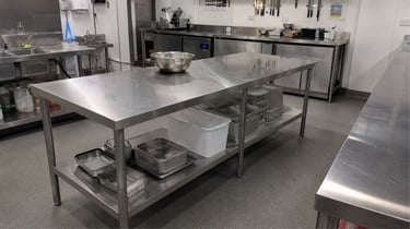 Stainless steel benches for commercial kitchens holding bowls and containers.
