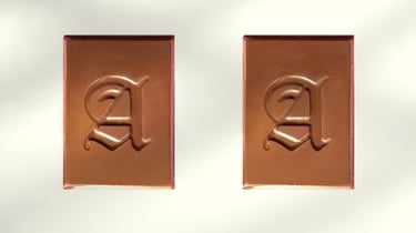 Two rectangles of chocolate rectangles featuring an embossed gothic letter A on a white background.