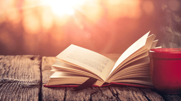 a book on a table outside with a cup of coffee