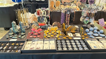 A display of gemstone jewelry, crystal towers, and mineral specimens at a gem and mineral show booth.