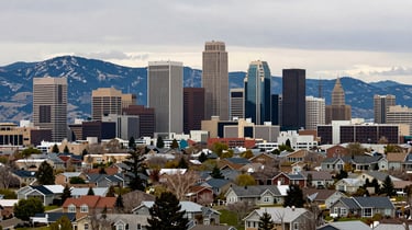 Wide panoramic shot of Salt Lake City skyline from a hillside neighborhood, downtown towers visible, Wasatch range behind, natural overcast daylight, residential streets in foreground