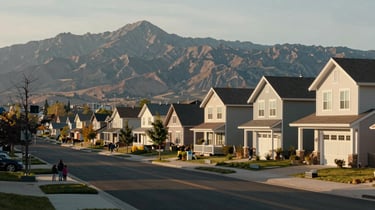 West Valley City Utah neighborhood street, mix of established homes and new builds, families visible on sidewalk, Oquirrh Mountains in background, warm afternoon light