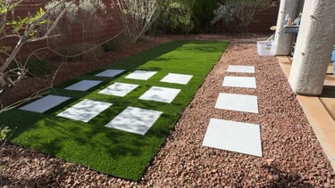Backyard with a checkered pattern of synthetic grass and decorative rocks, showcasing a clean.