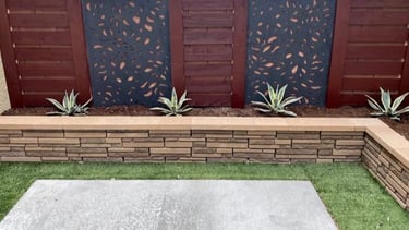 Small decorative retaining wall made of concrete blocks surrounding a garden bed in a backyard patio