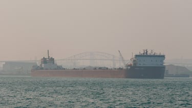 Huge red freighter Stewart J. Cort approaching. The sky is hazy with wildfire smoke.