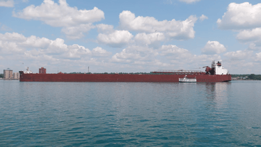 Small Soo Locks tour boat next to huge red freighter James R. Barker.