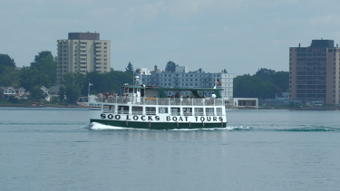 A green and white Soo Locks tour boat passing by on the St. Marys River.