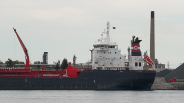 Aft section of a blue and white tanker ship, moored in front of a smokestack.