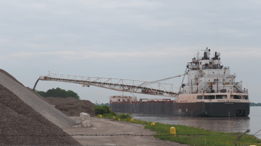 A stern view of freighter American Courage unloading stone onto a large pile.