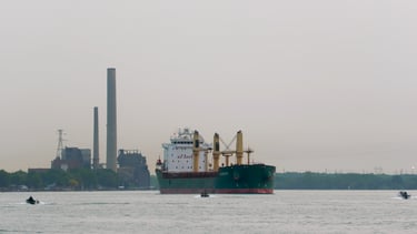 Green and white oceangoing ship with yellow deck cranes, passes 2 small boats.