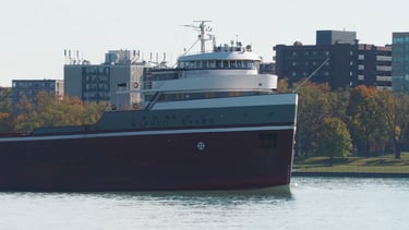 Close-up of the forward pilothouse of freighter Wilfred Sykes passing apartment buildings.