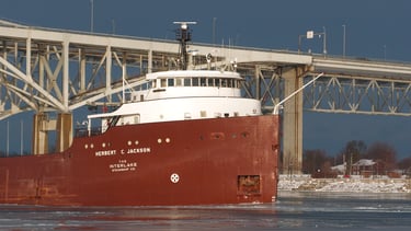 Close-up of the forward pilothouse of a classic red and white freighter passing a bridge.