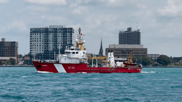 Port side view of red and white Canadian Coast Guard vessel Limnos passing some buildings.