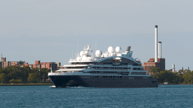 A blue and white cruise ship passing. Apartment buildings and some smokestacks in the background.