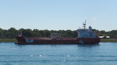 Left side view of a red tanker ship with a white superstructure and 2 white stripes near the bow.