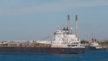 Aft section of a black and white freighter passing 2 smokestacks.