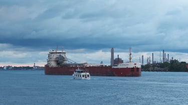 A small tour boat passing a large red and white ship under dramatic looking clouds.