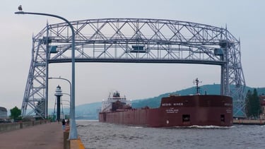 A huge red ship passing under the Duluth Aerial Lift Bridge.