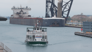 A Soo locks tour boat passes a huge freighter that is pulling into the Poe Lock.