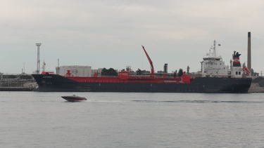 A small fishing boat speeds past a blue tanker ship that is moored.
