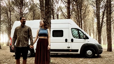 casal sorrindo na floresta em frente a um motorhome