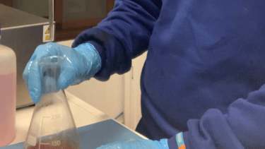 a man in a blue shirt and gloves is holding a bottle of liquid
