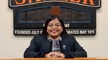 a woman in a black jacket and glasses sitting at a podium