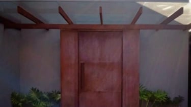 Porta de entrada pivotante de grandes dimensões, com revestimento que imita a aparência enferrujada do aço corten, sob uma pé