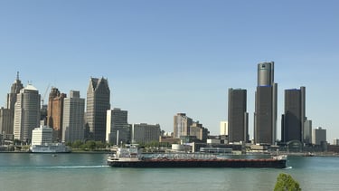 A black and white ship passing the downtown Detroit skyline.