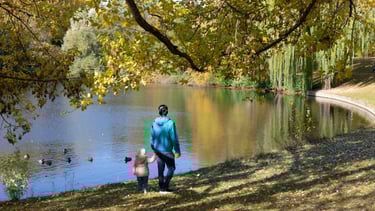 Bild von einer erwachsenen Person, die mit einem Kind an der Hand an einem See spazierengeht.
