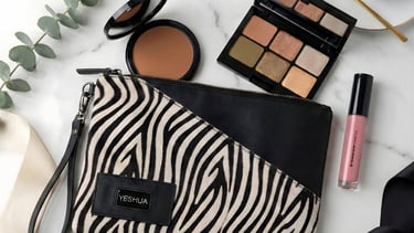 Zebra print makeup bag with eyeshadow palette, lip gloss, and bronzer on a marble surface.