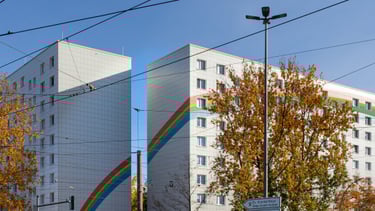 Bild von zwei nebeneinanderstehenden weißen Hochhäusern mit aufgemaltem Regenbogen.