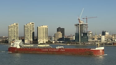 A red and white ship passes by buildings of the Detroit skyline.