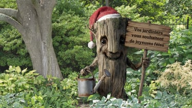 PLV, décoration. Un personnage en tronc d'arbre en PVC qui tient une pancarte dans un jardin.