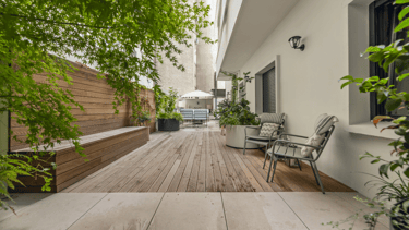 Espacio del jardín con suelo de gres estilo madera, fachada blanca y muro recubierto con madera.