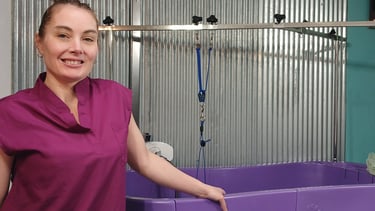 a dog groomer in a purple shirt is standing in front of a tub