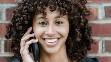 a woman with curly hair and a gray jacket.  She's smiling and talking on the phone.